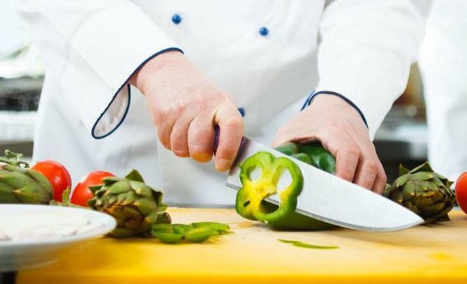 Na zdjęciu kucharz kroi paprykę i karczochy