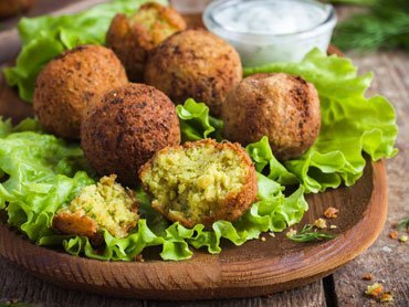 Zdjęcie przedstawia udekorowany sałatą drewniany talerz, na nim kilka falafli z podagrycznikiem