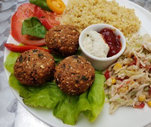 Zdjęcie przedstawia talerz z falaflami z podagrycznikiem podane z kaszą, surówką, warzywami i sosami
