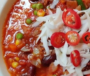 Na zdjęciu talerz, na nim potrawa Chilli con Bulgur podana z tartą vegańską mozzarellą