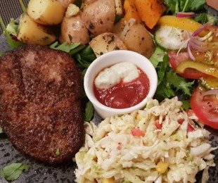 Na zdjęciu talerz, na nim Quorn Stek podany z pieczonymi ziemniakami, surówką, warzywami i sosami