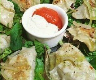 Zdjęcie przedstawia talerz z pierogi z pokrzywą i sosierkę z dwoma sosami