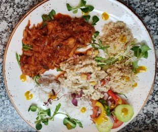 Na zdjęciu talerz, na nim potrawa Pulled Jackfruit podany z kaszą, ryżem, warzywami i surówkami