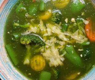 Zdjęcie przedstawia talerz bulionu jarmużowego z warzywami i tartym serem