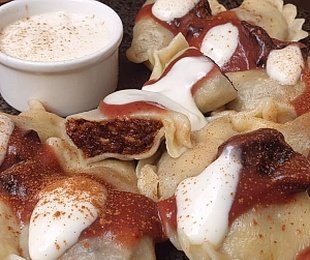 Na zdjęciu talerz, na nim Pierogi orzechowo śliwkowe podany z sosem śliwkowym i wegańską śmietanką