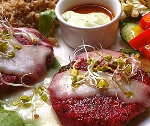 Na zdjęciu talerz, na nim dwa kotlety buraczane podane z kaszą, warzywami i sosami