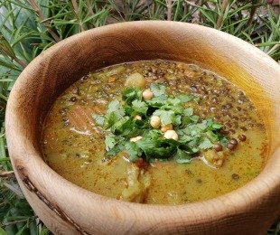 Zdjęcie przedstawia drewnianą miskę zupy Kokosowe Curry z czarnej soczewicy, posypanej świeżą kolendrą