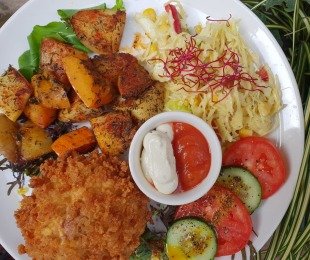 Na zdjęciu talerz, na nim Pieczarka Portobello w panierce podana z pieczonymi ziemniakami, surówką, warzywami i sosami