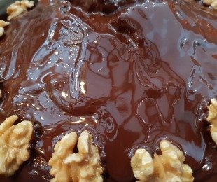 Zdjęcie przedstawia ciasto, piernik w czekoladzie udekorowany orzechami